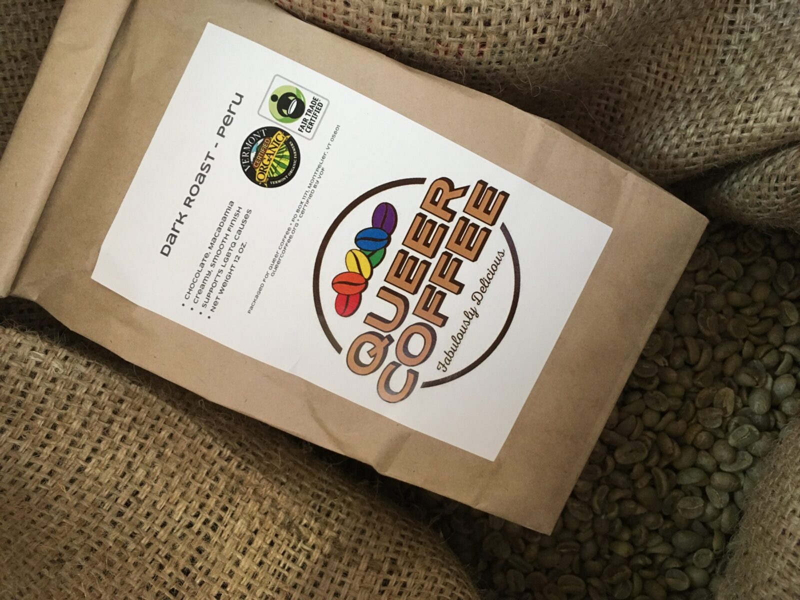 Bag of Queer Coffee nestled in a burlap bag of coffee beans.